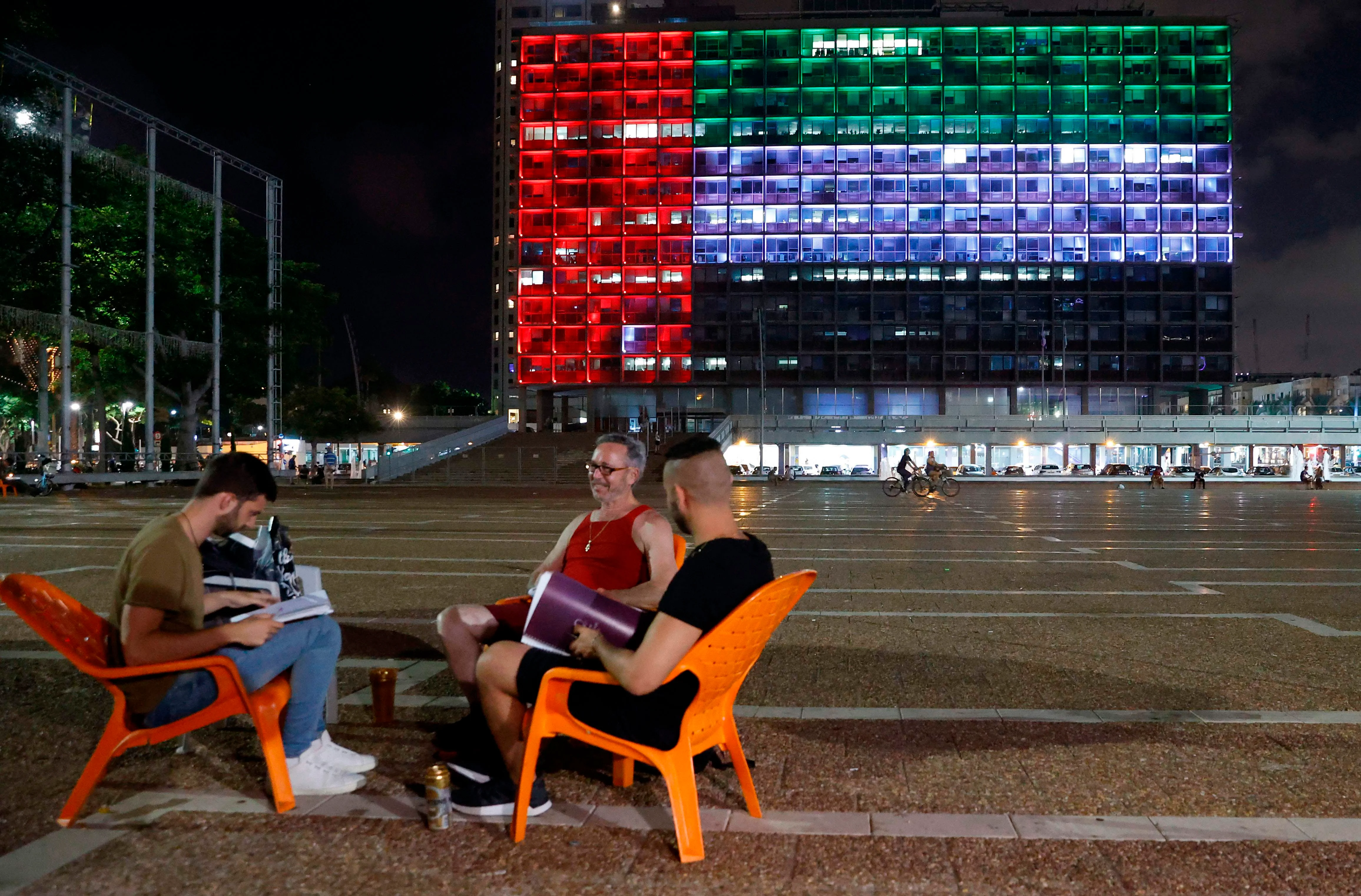 People enjoy a drink in Tel Aviv, Israel as a building in the area gets illuminated with the UAE flag, following the peace deal