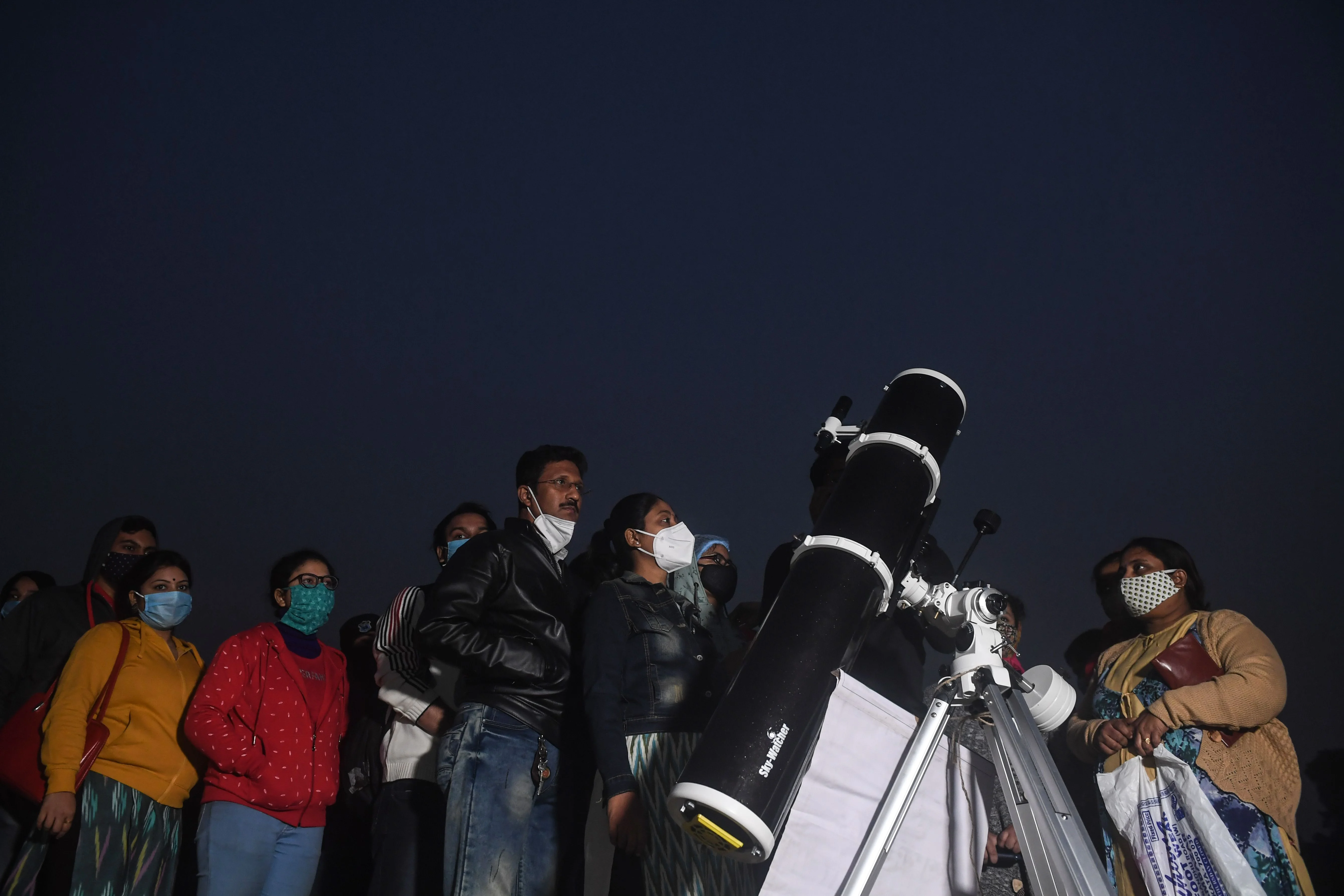 People stand in a queue to see a great conjunction of Jupiter and Saturn at the Maidan area in Kolkata on December 21, 2020.
