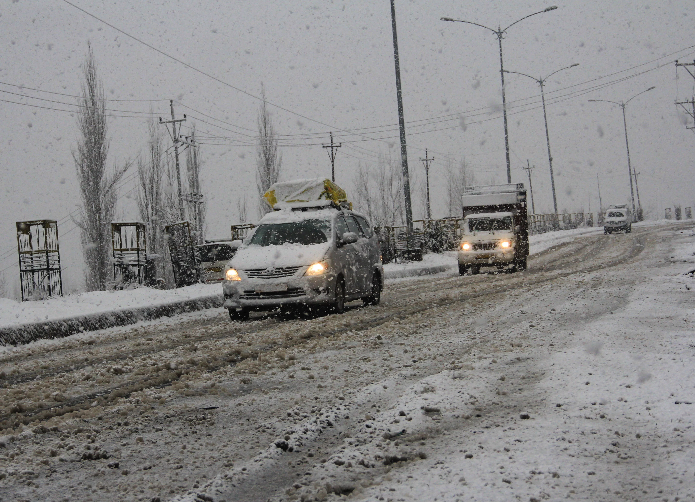 Vehicles move through a snow-covered road during a snowfall in parts of Kashmir on Saturday