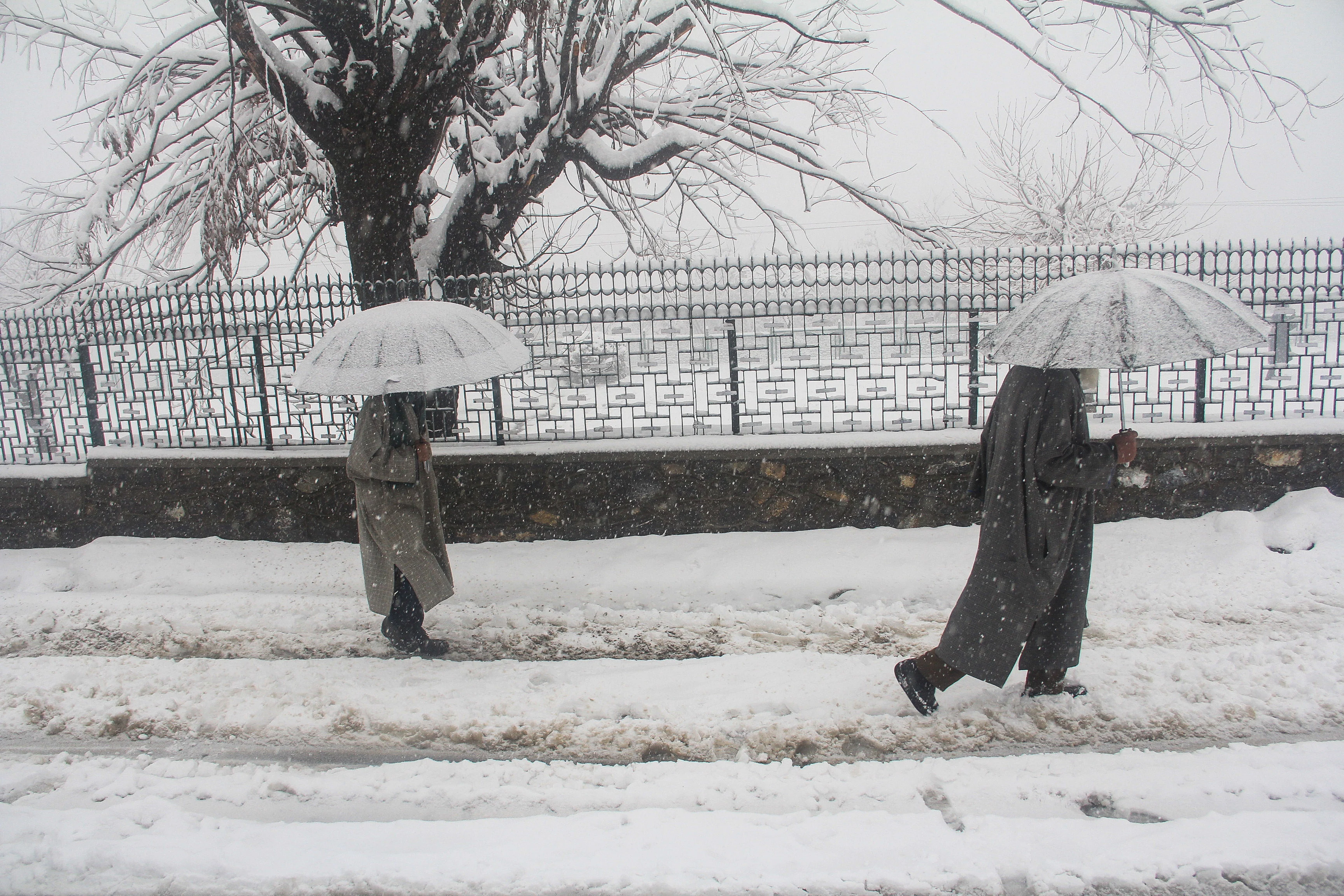 Pedestrians walk across a snow-covered road in Baramulla District of Jammu and Kashmir, on Saturday.