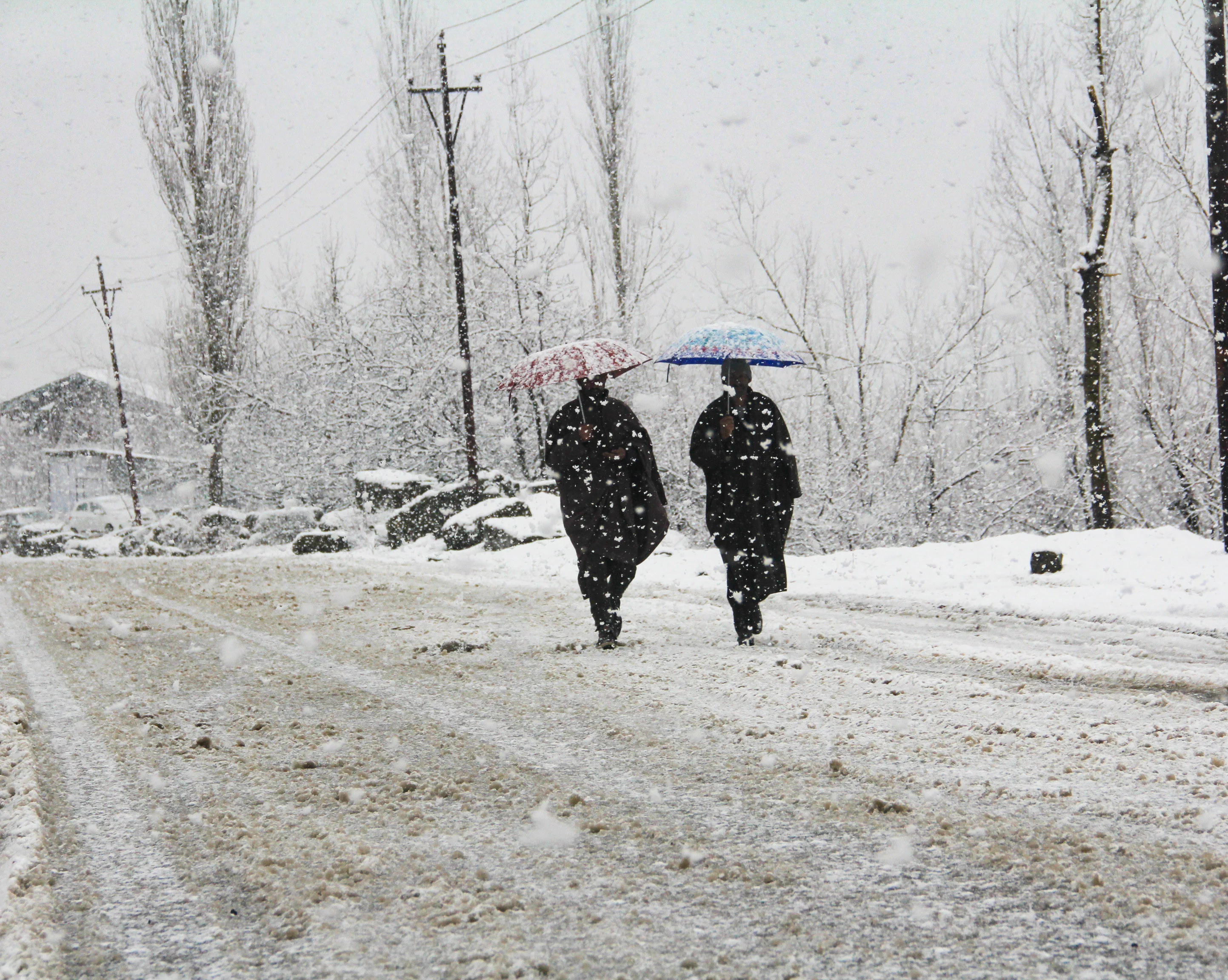Pedestrians walk across a snow-covered road in Baramulla District of Jammu and Kashmir, on Saturday.