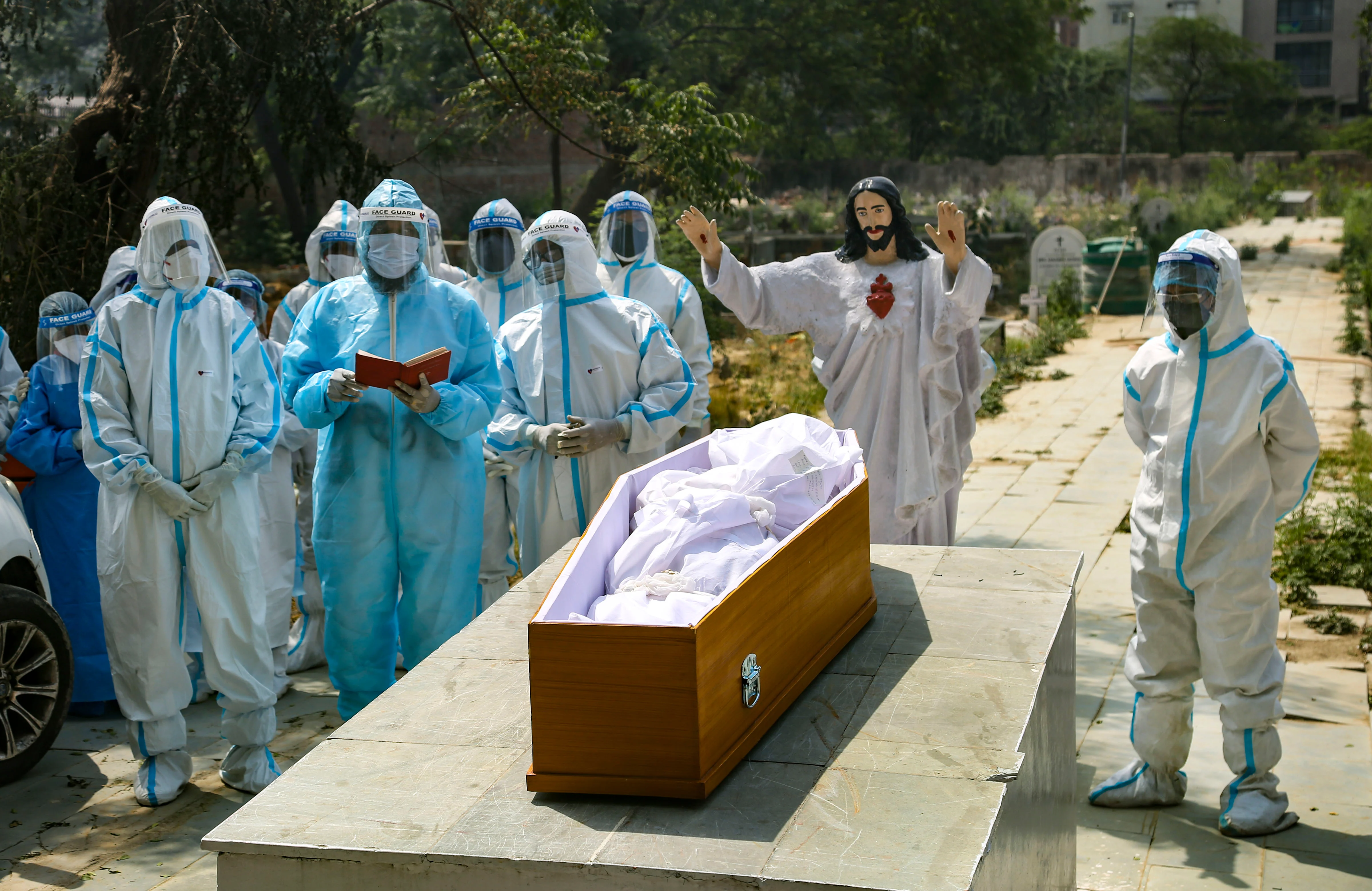 A priest reads the bible during the last rites of a person who died of coronavirus, at a Christian cemetery in New Delhi, Tuesday, April 27, 2021.