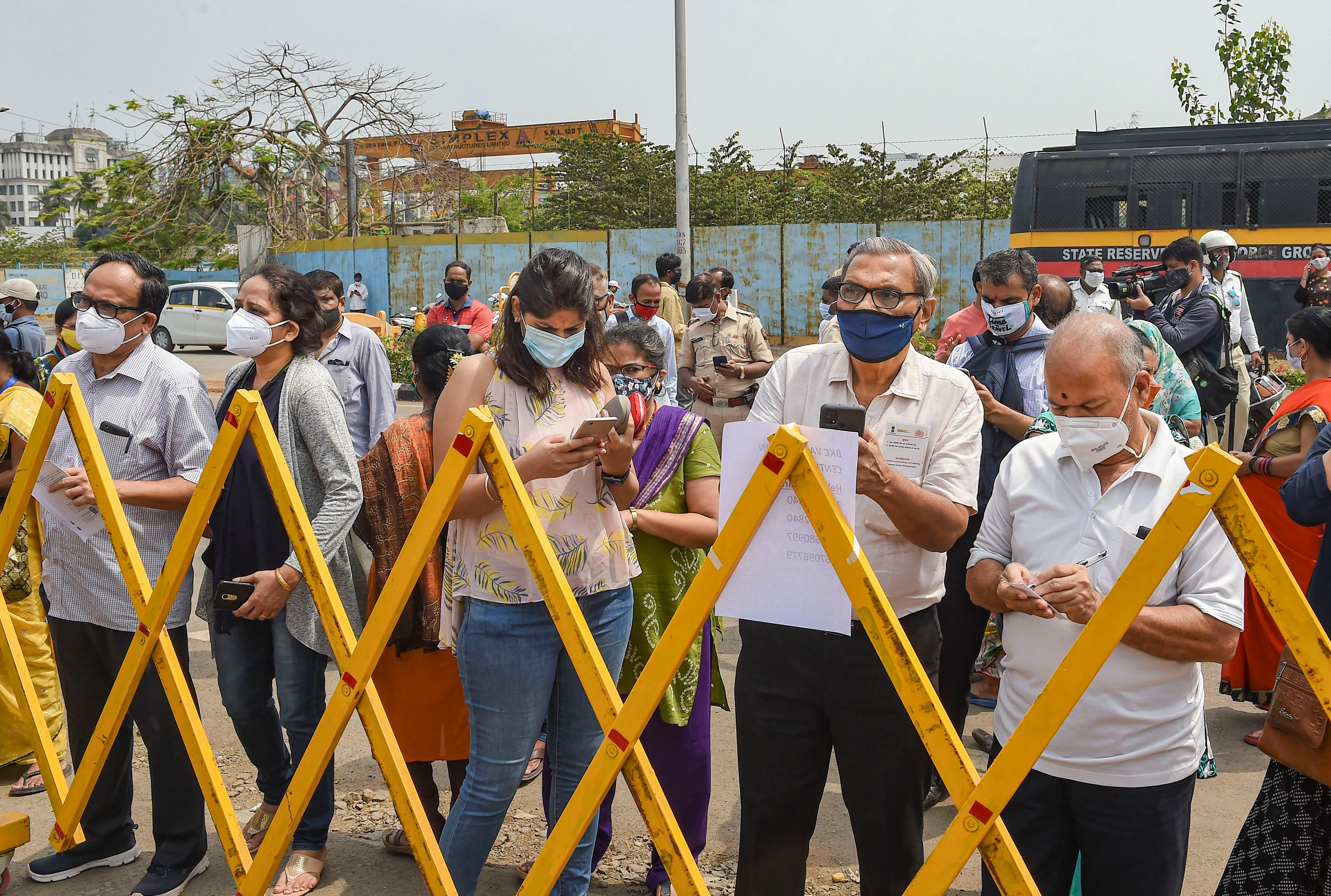 People stand behind a barrier outside a Covid-19 vaccination centre as vaccination was stopped due to shortage of vaccine supplies, in Mumbai, on April 9, 2021