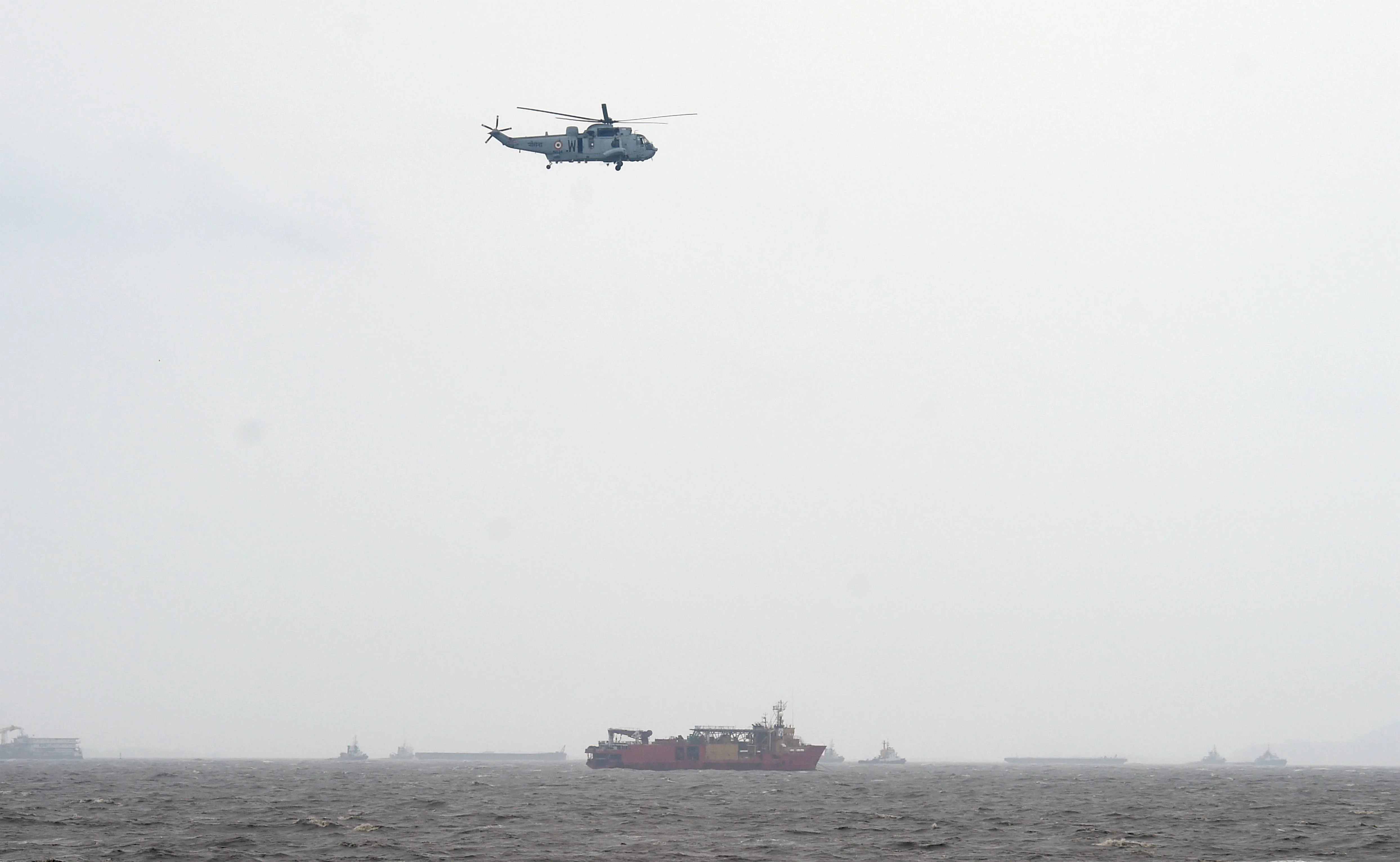 A helicopter flys over a ship anchored in the rough Arabian Sea near Mumbai