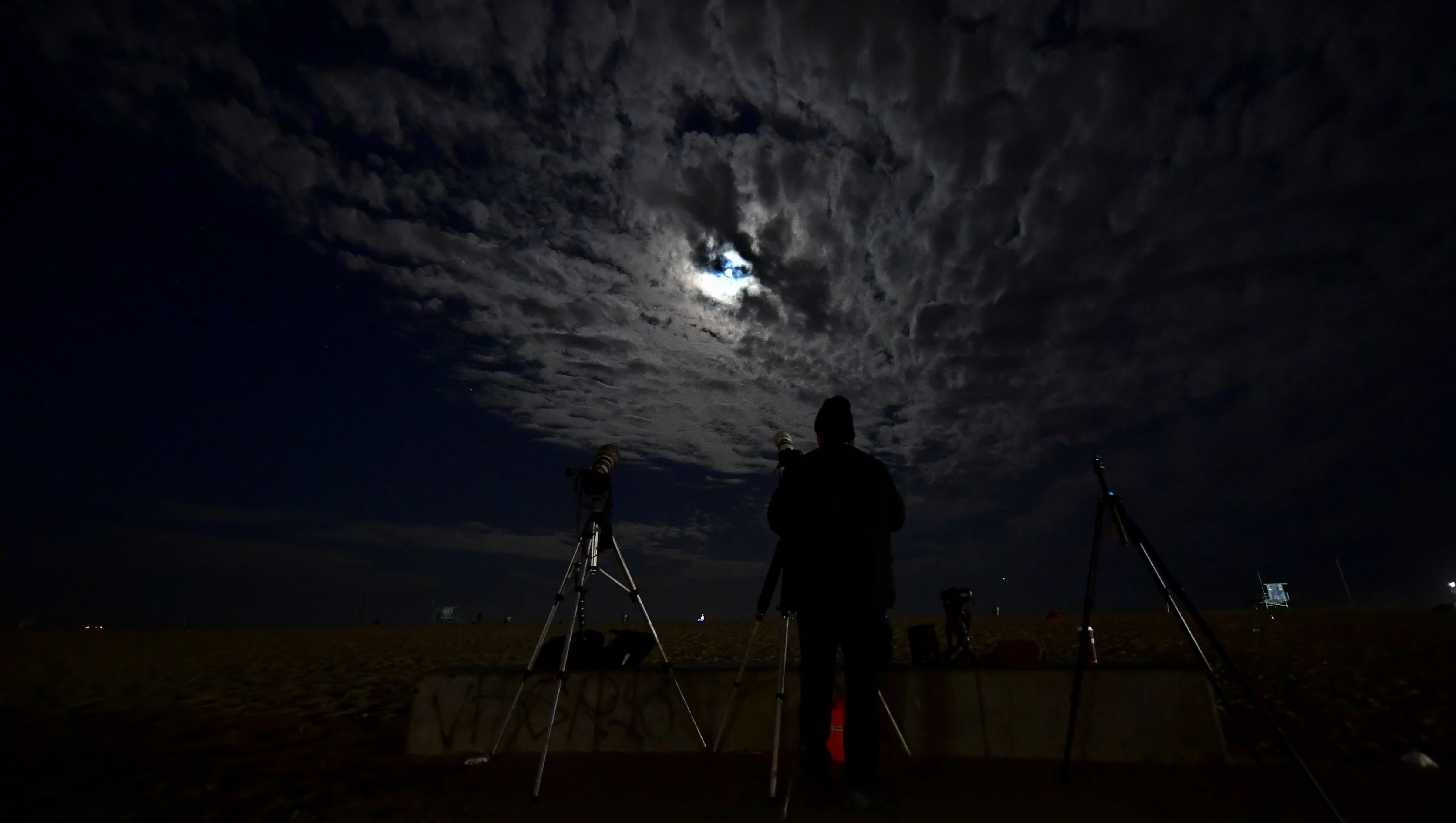 Clouds cover the Moon as a photographer views it from Santa Monica, California ahead of a total lunar eclipse early on May 26, 2021, as stargazers across the Pacific are casting their eyes skyward to witness a rare "Super Blood Moon".