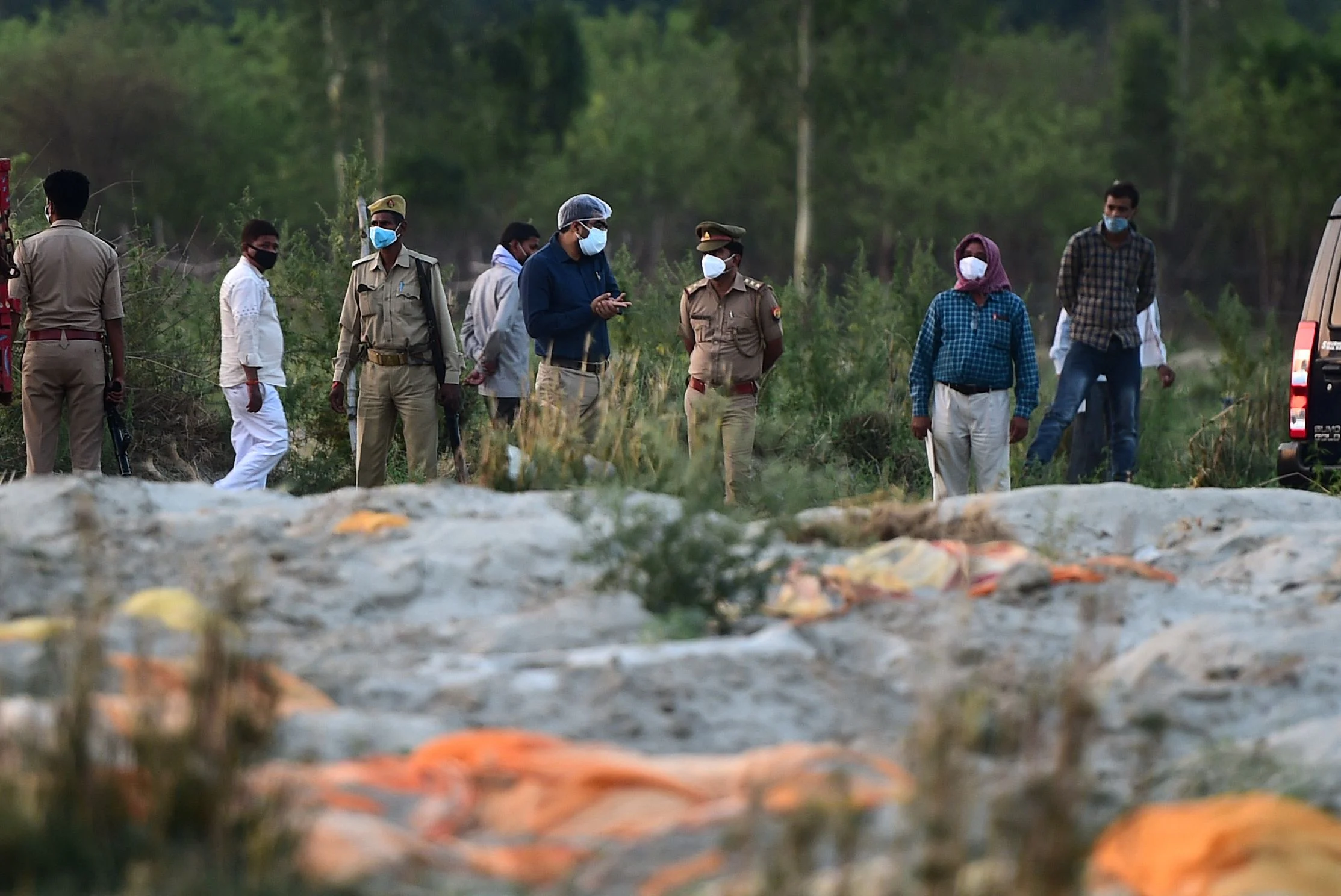 Police and administrative officials (background) inspect a cremation ground on the banks of Ganges River, where suspected bodies (foreground) of Covid-19 coronavirus victims appeared partially buried, at Rautapur Ganga Ghat in Unnao on May 13, 2021.