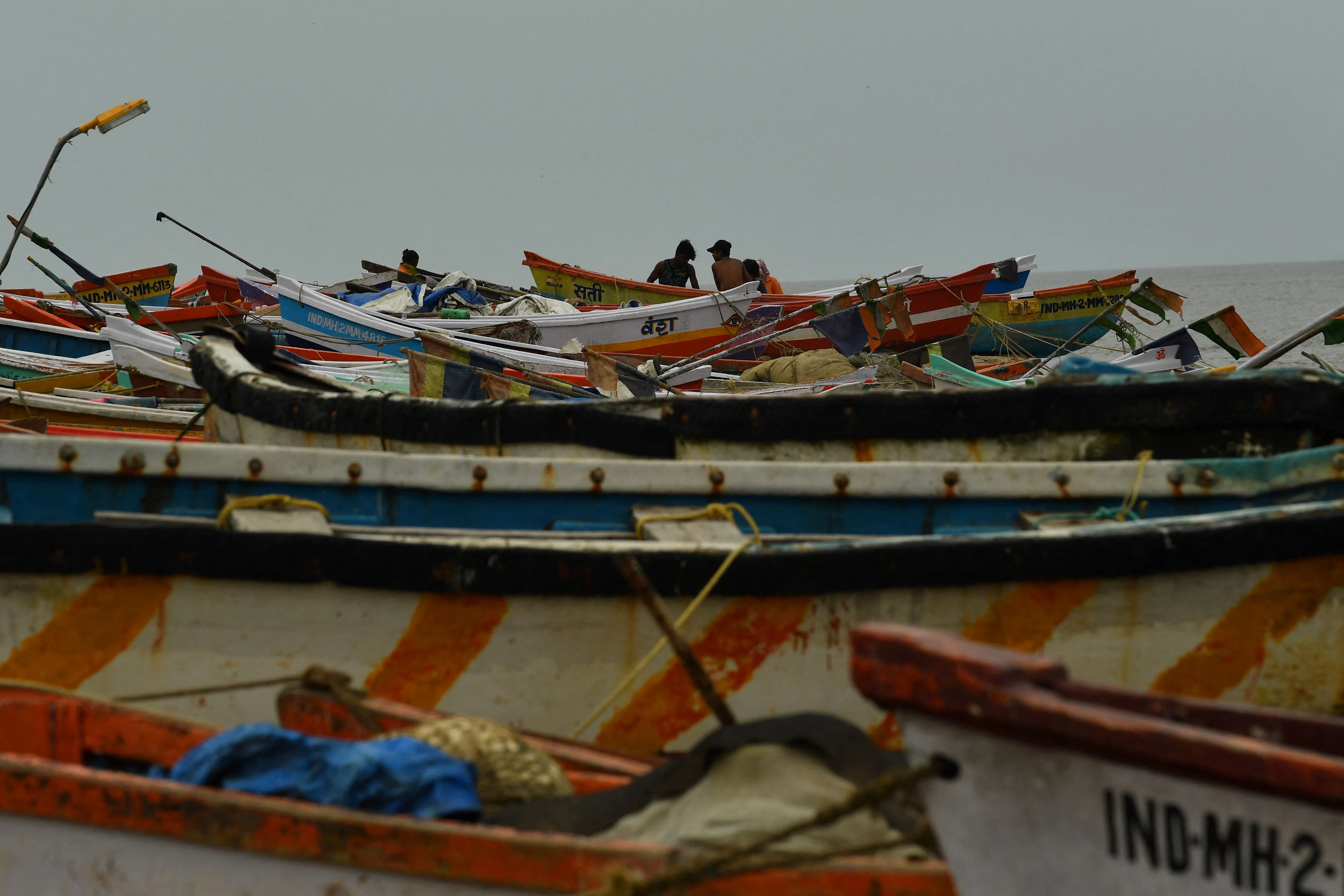 Fishermen are seen next to boats being moored at a fishing village off the city coast in the wake of the impending cyclone Tauktae in Mumbai on May 16, 2021.