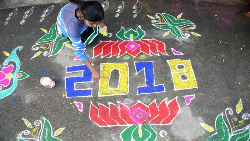 A woman applies coloured powder to a “rangoli”, a Hindu ritual design, to usher in the New Year in front of a home in Hyderabad on January 1, 2018. / AFP PHOTO / Noah SEELAM
