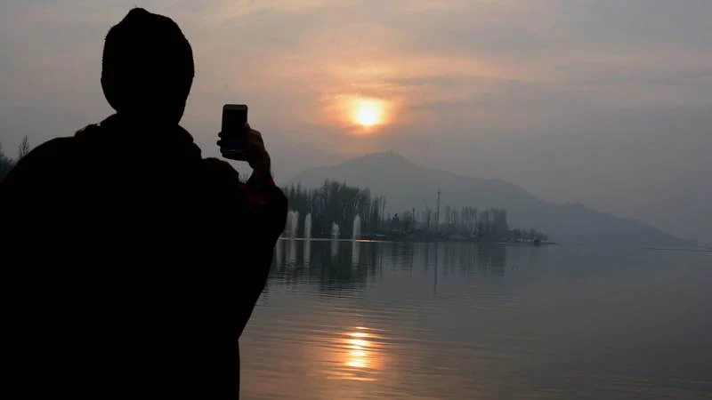 A youth uses his mobile phone to capture the pictures of last sunset of year-2017, at Dal Lake in Srinagar on Sunday. PTI Photo