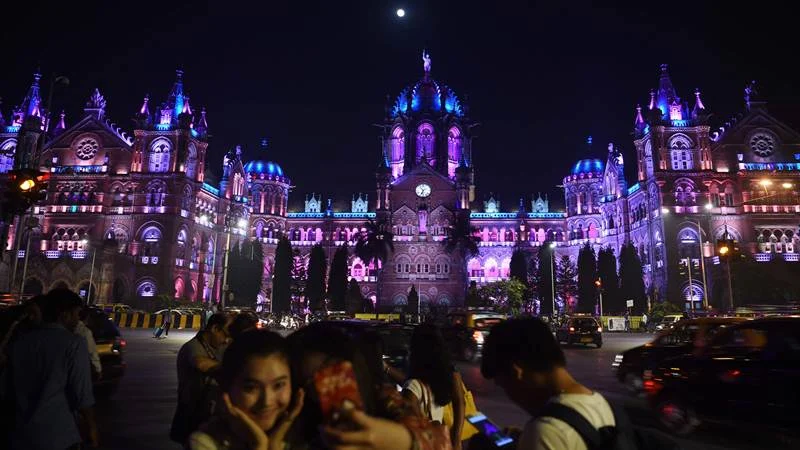 Indians take pictures in front of the lit up Chattrapathi Shivaji Terminus (CST) railway station ahead of New Year’s eve. / AFP PHOTO / PUNIT PARANJPE