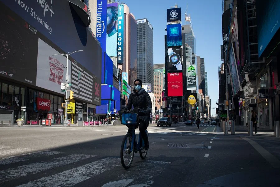 A person wearing a face mask rides a bicycle at Times Square in New York, the United States, on March 26, 2020.