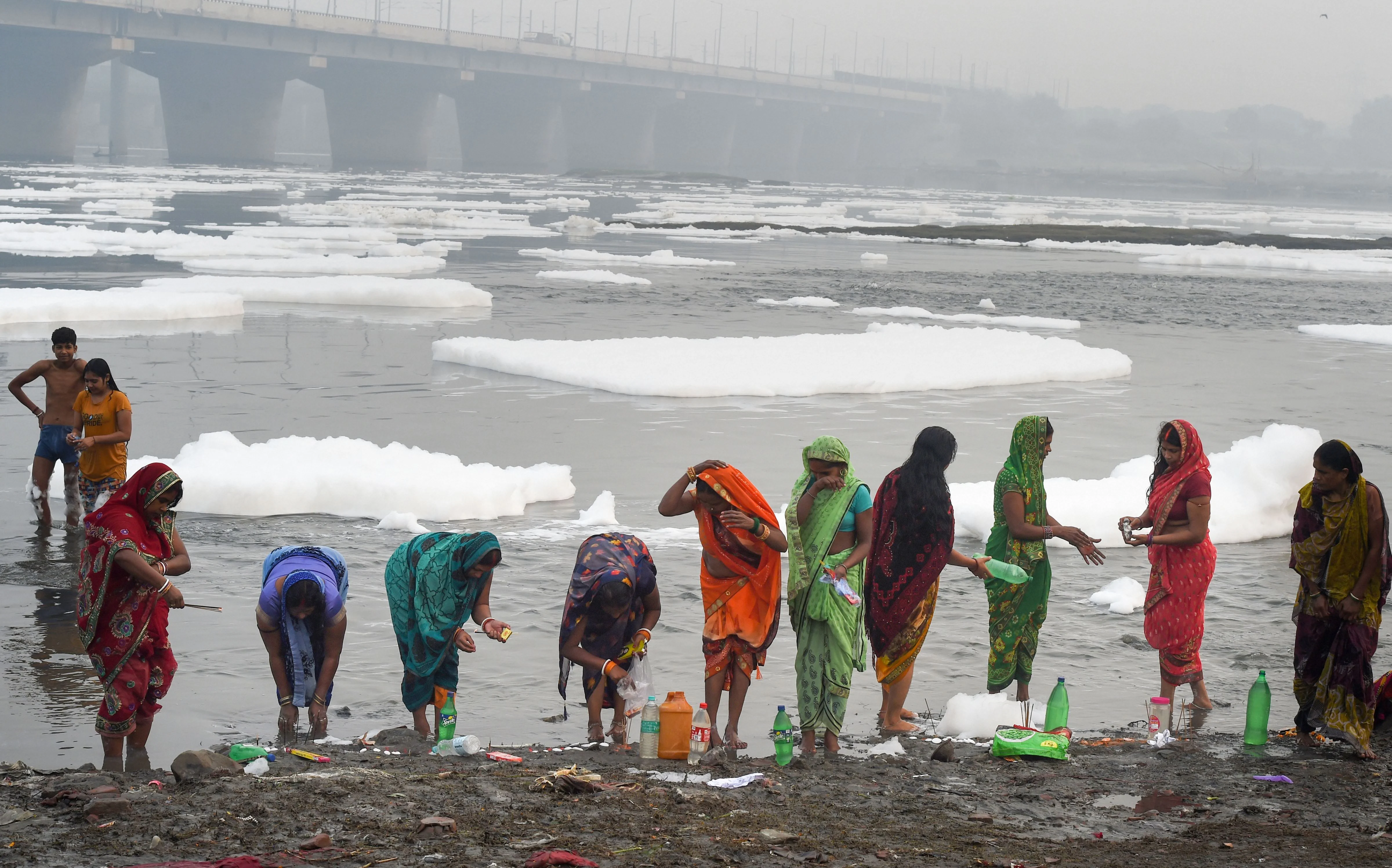 Hindu devotees perform rituals of four days long Chhath Puja celebration, as toxic for floats on the surface of polluted Yamuna river at Kalindi Kunj, in New Delhi, Sunday, Nov. 7, 2021.
