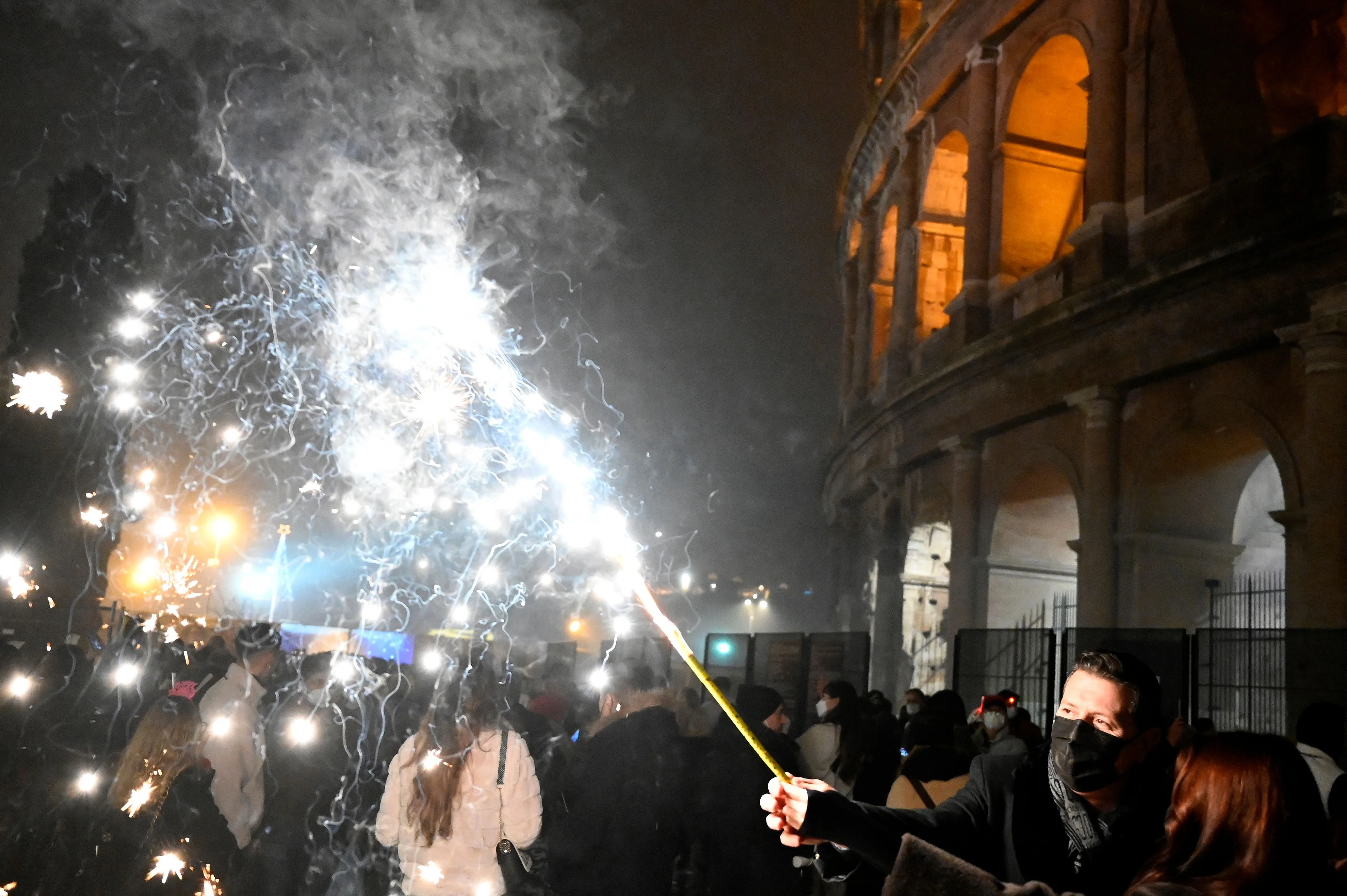 People hold a lit sparkler on New Years Eve outside the Colosseum in Rome on December 31, 2021.