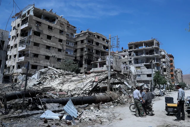 People stand in front of damaged buildings, in the town of Douma, the site of a suspected chemical weapons attack, near Damascus, Syria. Two days after Syrian troops declared Douma liberated from opposition fighters, a tour in the city showed the widespread destruction it has suffered since falling under rebel control six years ago People stand in front of damaged buildings, in the town of Douma, the site of a suspected chemical weapons attack, near Damascus, Syria. Two days after Syrian troops declared Douma liberated from opposition fighters, a tour in the city showed the widespread destruction it has suffered since falling under rebel control six years ago