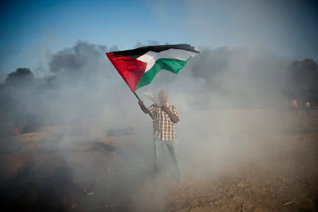 A Palestinian protester wears a plastic bag on his head as a protection from teargas, waves a national flag during a protest at the Gaza Strip’s border with Israel. Violence erupted at the Gaza border. A Palestinian protester wears a plastic bag on his head as a protection from teargas, waves a national flag during a protest at the Gaza Strip’s border with Israel. Violence erupted at the Gaza border.