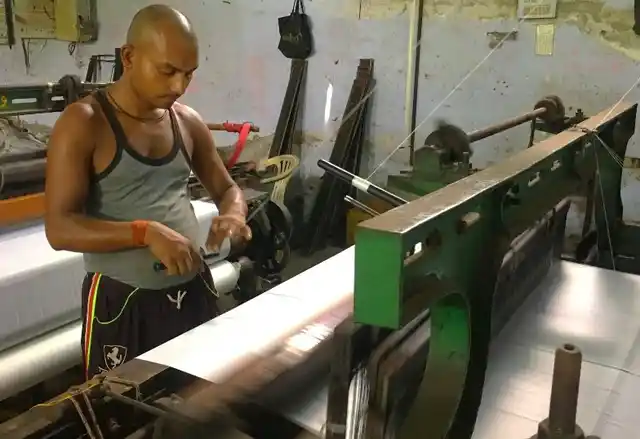 A part time worker at a power loom unit does his job.