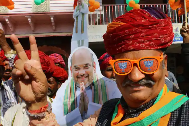 A Bharatiya Janata Party (BJP) supporter displays a victory sign in front of the cutout of BJP President Amit Shah during an election rally.