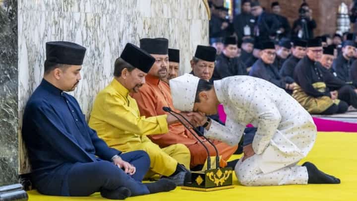 This handout picture taken by Brunei’s Information Department on 11 January 2024 and released on 12 January 2024 shows Brunei’s Prince Abdul Mateen (R) touching his forehead on his father’s hand, Brunei’s Sultan Haji Hassanal Bolkiah (2nd L), after his solemnization at Sultan Omar Ali Saifuddien Mosque in Bandar Seri Begawan. (Photo by Handout / Brunei’s Information Department / AFP)