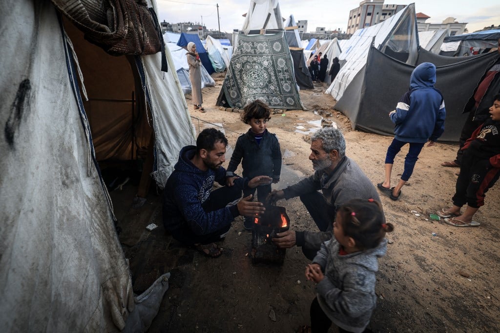 Displaced Palestinians try to warm up around a fire amid tents flooded by heavy rain, at a makeshift camp set up by people who fled the ongoing battles between Israel and Hamas militants, in Rafah in the southern Gaza Strip on January 27, 2024.
