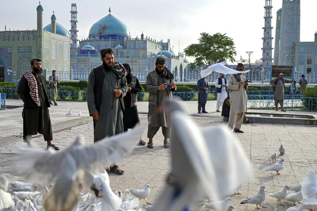 (FILES) In this photograph taken on 3 June 2023, Afghan men walk past pigeons at the Shrine of Hazrat Ali or Blue Mosque, in Mazar-i-Sharif.
