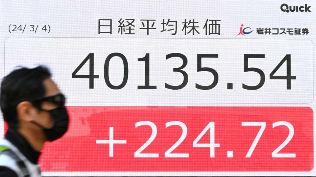 A man walks past an electronic board displaying a share price of the Nikkei index of the Tokyo Stock Exchange above 39,000 points on a street in Tokyo on 4 March 2024.