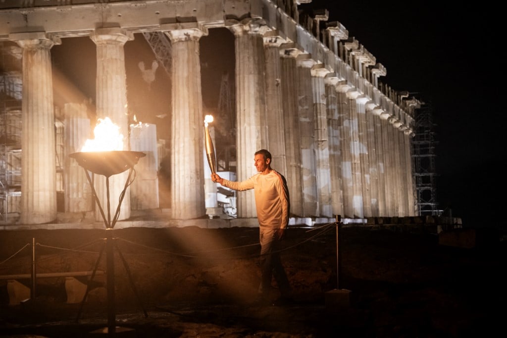 Greek 400-meter champion Periklis Iakovakis holds the Olympic flame in front of the ancient temple of the Parthenon atop the Acropolis hill during the Olympic torch relay in Athens on 19 April 2024.
