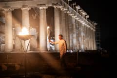 Greek 400-meter champion Periklis Iakovakis holds the Olympic flame in front of the ancient temple of the Parthenon atop the Acropolis hill during the Olympic torch relay in Athens on 19 April 2024.