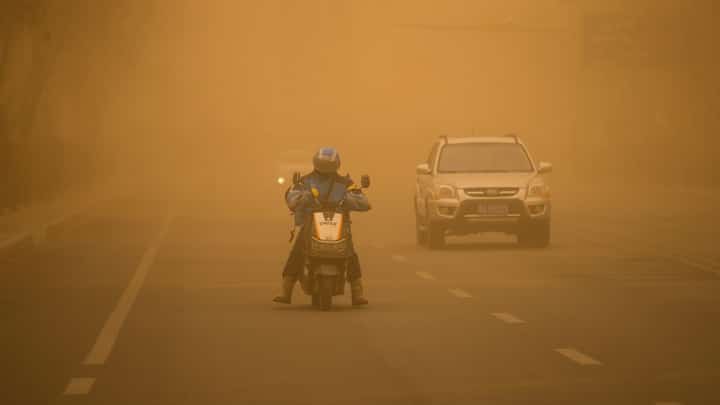 (FILES) This photo taken on 27 March 2024 shows people driving vehicles on a street during a sandstorm in Erenhot, in northern China's Inner Mongolia autonomous region.
