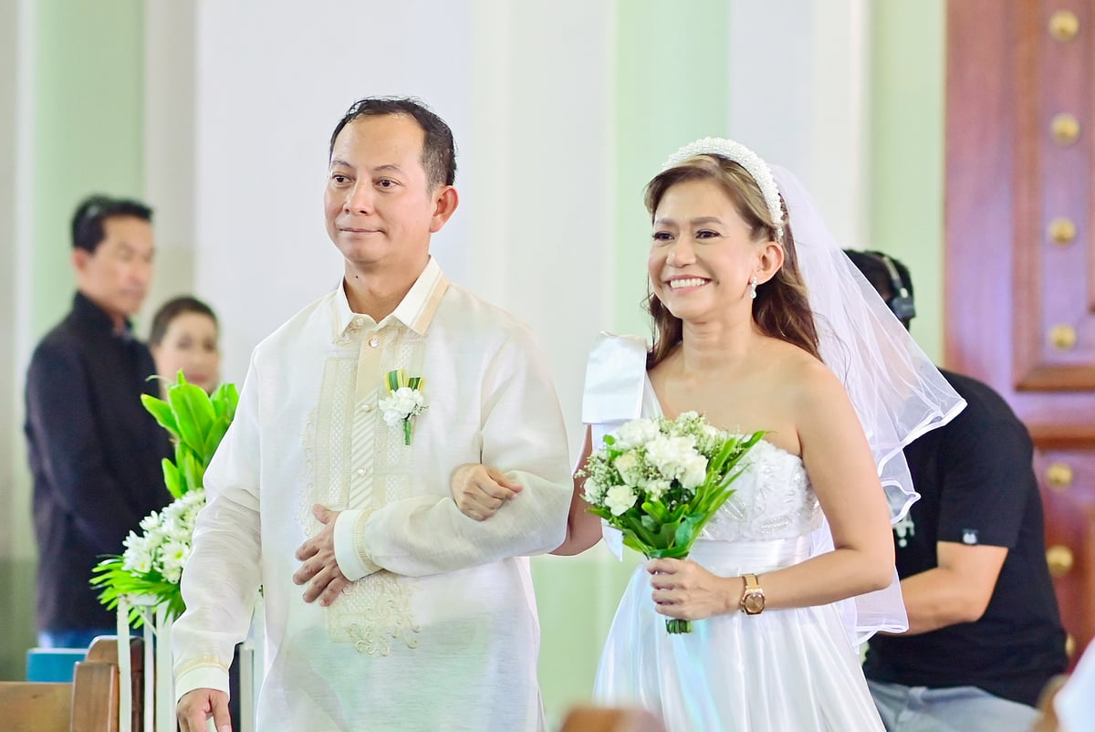 Susy Loma (right), radiant with her hair and makeup provided by Gandang Ricky Reyes to all 16 couples, walks the aisle with her husband Arturo Regis (left).