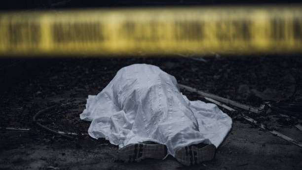 Dead body under a white sheet of cloth behind a police line