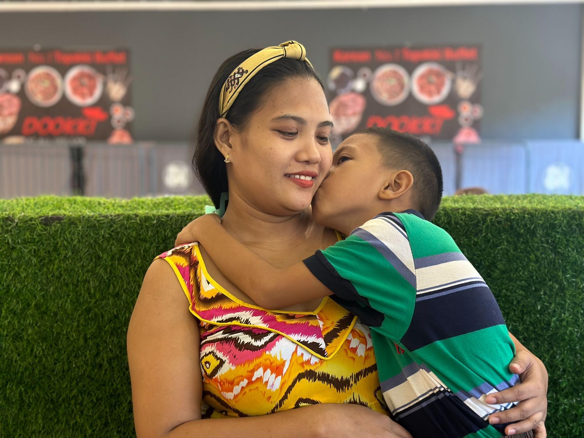 Regina’s seven-year-old son gives her a kiss, thanking her for taking care of him.