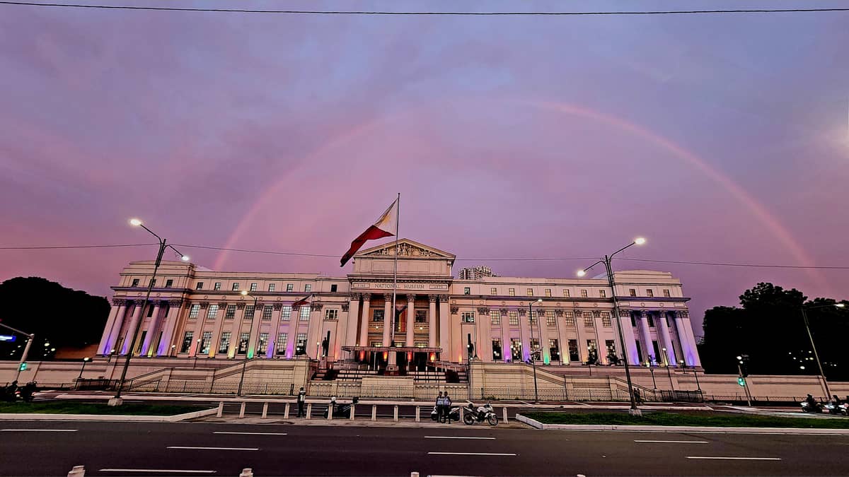 A rainbow appears over the National Museum of Fine Arts as the National Museum of the Philippines unfurls a Progress Pride Flag and lights the facade with rainbow colors.
