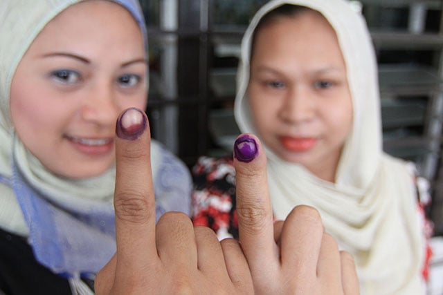 Two women wearing headscarves show their ink-stained index fingers as proof of voting participation in the Philippine elections.