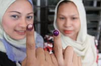 Two women wearing headscarves show their ink-stained index fingers as proof of voting participation in the Philippine elections.