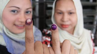 Two women wearing headscarves show their ink-stained index fingers as proof of voting participation in the Philippine elections.