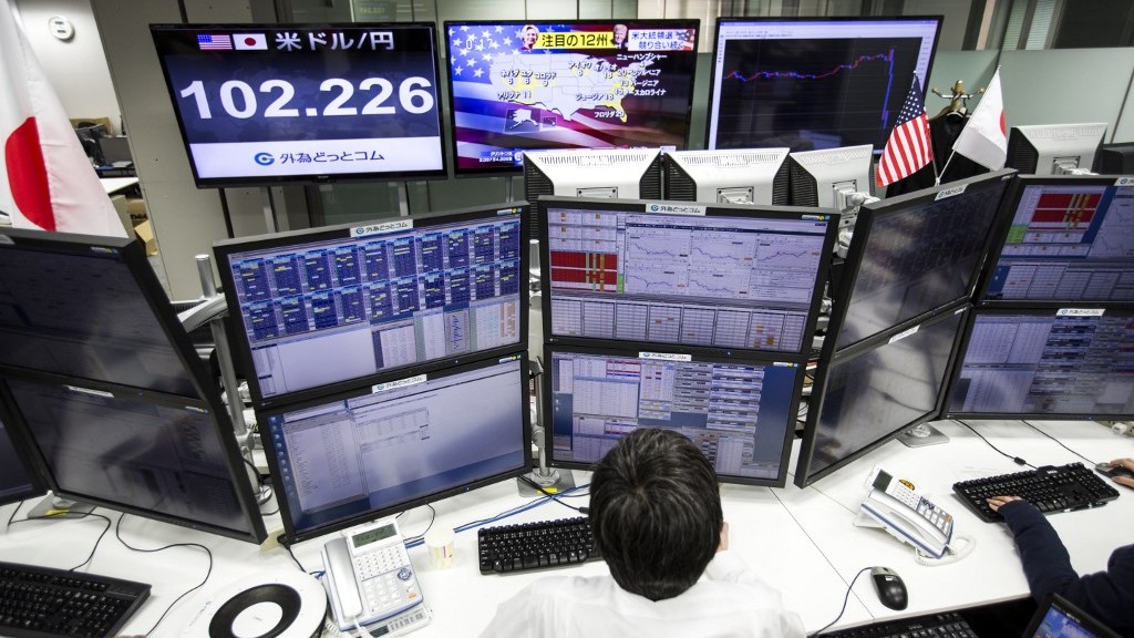 (FILES) A Japanese employee of a foreign exchange trading company works next to screens displaying the latest US presidential election results on TV news channels, and the Japanese yen's exchange rate against the US dollar (L) in Tokyo on 6 November 2016.