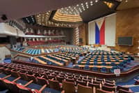 Wide view of the plenary hall of the Philippine House of Representatives at the Batasang Pambansa Complex, with empty seats and a large Philippine flag displayed at the front.