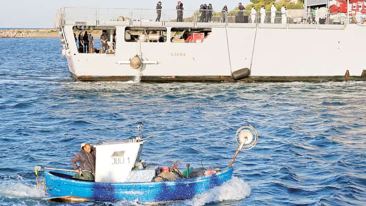 Fishing boat motors past a navy boat carrying migrants intercepted in Italian waters at Shengjin port in Albania on 16 October, 2024.