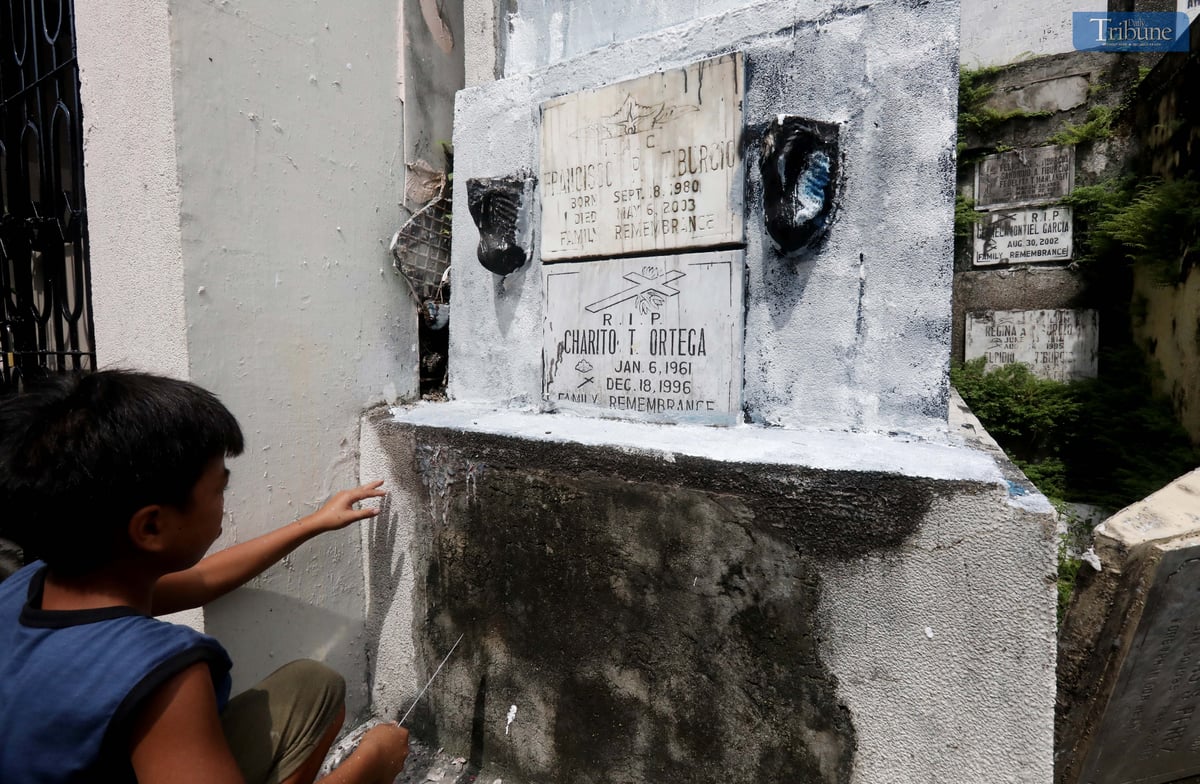 A young boy repaints the tomb of his departed grandmother and uncle at San Juan City Cemetery on Monday, October 28, 2024, in preparation for All Souls' Day.