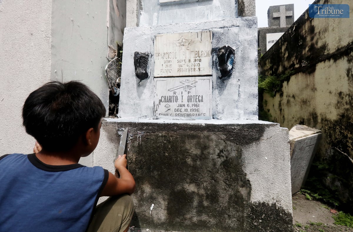A young boy repaints the tomb of his departed grandmother and uncle at San Juan City Cemetery on Monday, October 28, 2024, in preparation for All Souls' Day.