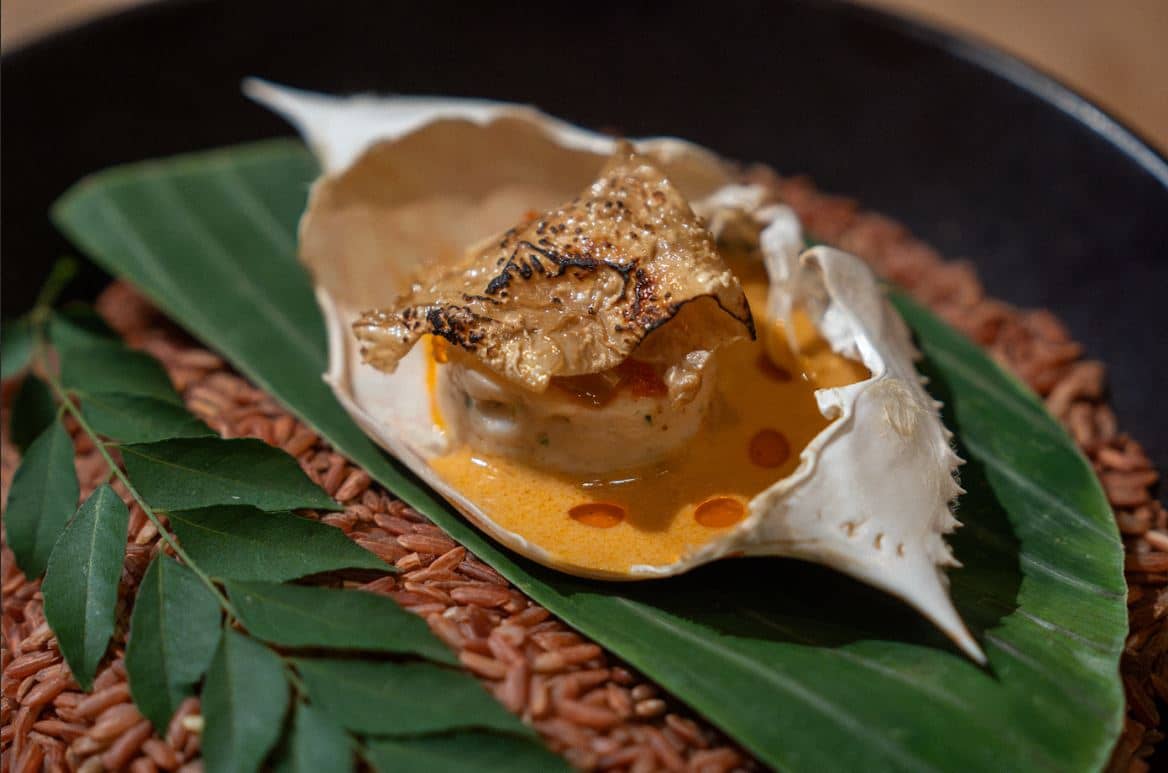 Crab and gabi leaf mousseline topped by gratinated soy film, moringa and finished with a coconut lemongrass annato sauce and curry leaf chili oil.