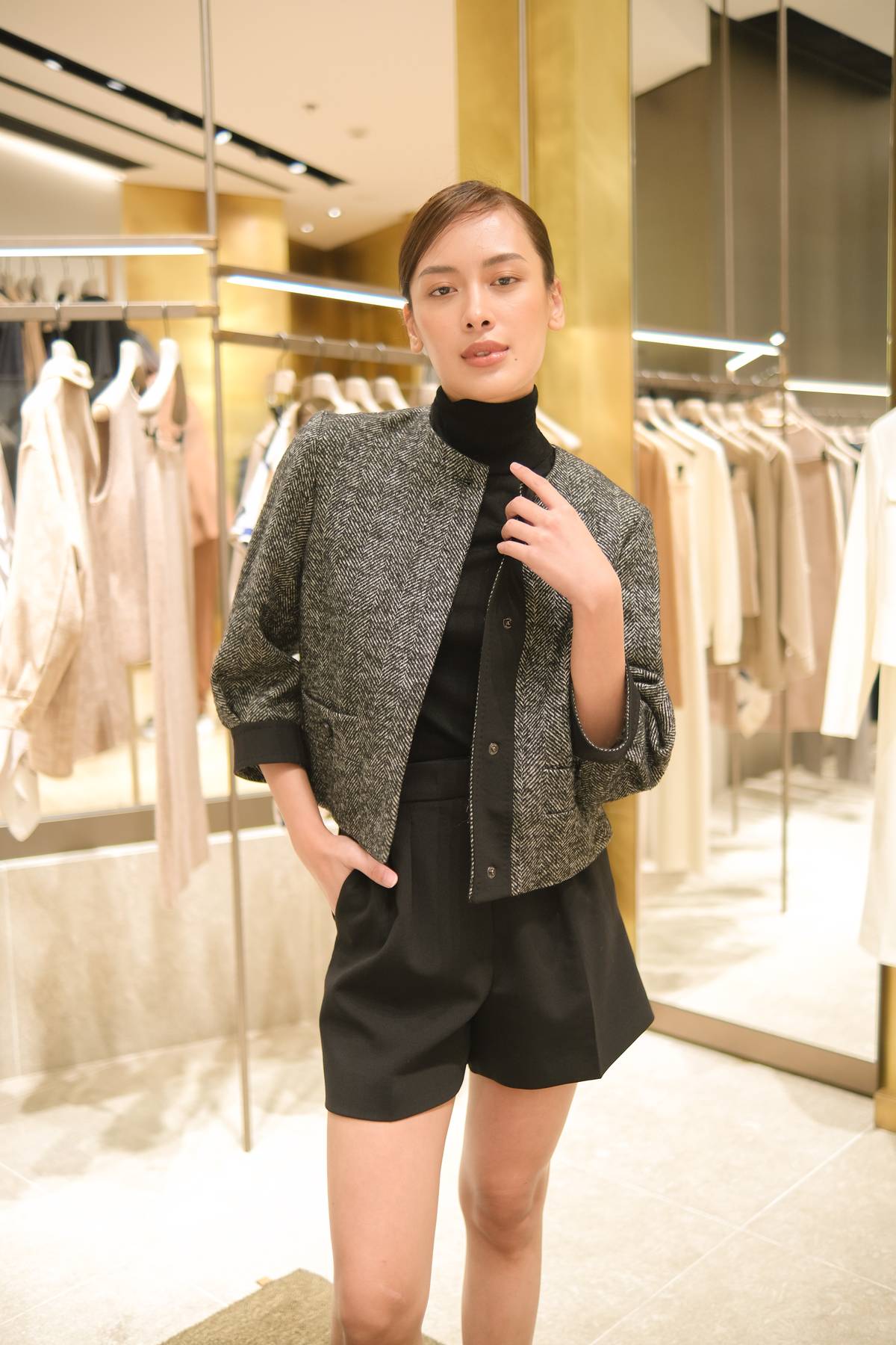 A gray jacket with a herringbone pattern, made of wool, is worn with a black turtleneck sweater and black relaxed shorts for the city girl.