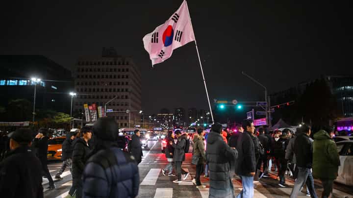 A man holds the South Korea flag outside the National Assembly in Seoul on 4 December 2024, after President Yoon Suk Yeol declared emergency martial law. South Korea's President Yoon Suk Yeol on 3 December declared emergency martial law, saying the step was necessary to protect the country from "communist forces" amid parliamentary wrangling over a budget bill.