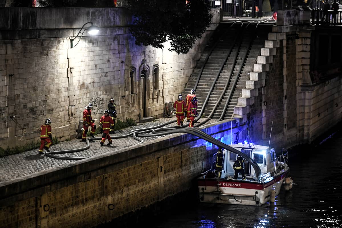 Firefighters assemble their hoses as they gather at the River Seine near Notre-Dame de Paris Cathedral as flames engulf the roof of the cathedral on 15 April 2019, in the French capital Paris.