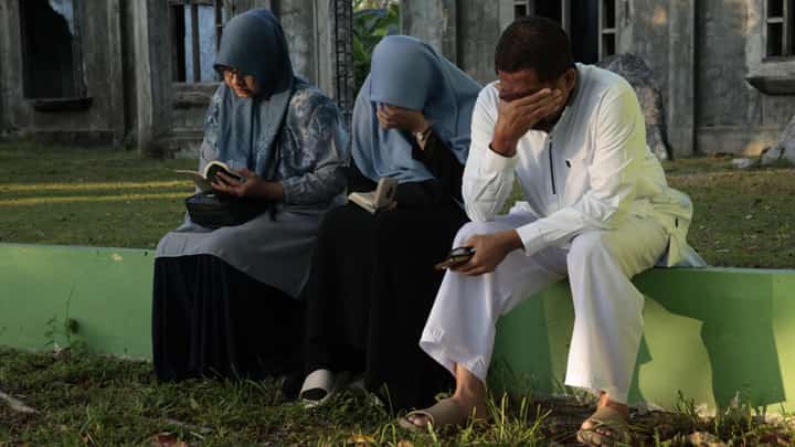 Mourners react as they gather at a mass grave in Indonesia's Aceh Province 20 years after the tsunami