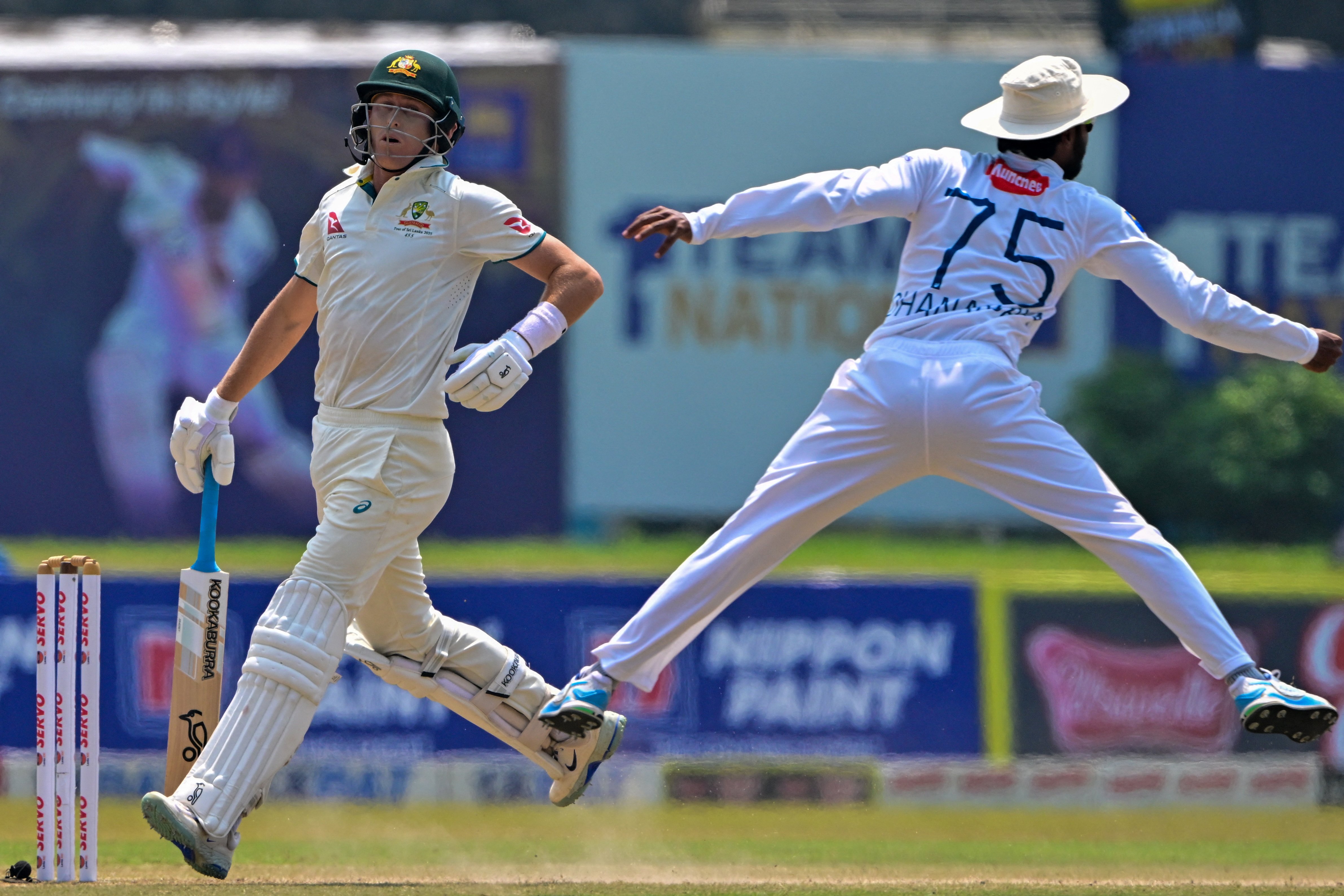Australia's Marnus Labuschagne (L) runs between the wickets as Sri Lanka's Dhananjaya de Silva jumps to field the ball during the fourth day of the second Test cricket match between Sri Lanka and Australia at the Galle International Cricket Stadium in Galle on 9 February 2025.