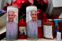 Candles with portraits of Pope Francis and Padre Pio are set at the bottom of a statue of Pope John Paul II outside the Gemelli Hospital where Pope Francis was hospitalized for tests and treatment for bronchitis in Rome, on February 19, 2025. Pope Francis, who has been diagnosed with pneumonia in both lungs, passed a "peaceful night", the Vatican said on 19 February 2025, amid growing concerns over the 88-year-old's condition.