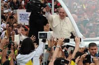 Pope Francis smiles and waves to a jubilant crowd of Filipino faithful during his visit to the Philippines, as hundreds raise their hands and phones to greet and capture the moment. Cardinal Luis Antonio Tagle is seen accompanying him in the popemobile.