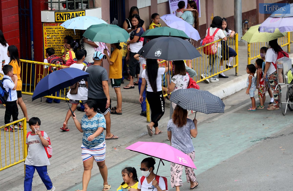 Students and their relatives shield themselves with umbrellas from the intense heat outside a school in Quezon City on Thursday, 6 March 2025. Due to the state weather bureau's forecast of "danger" and "extreme caution" heat index levels, some Luzon areas, including Metro Manila, suspended face-to-face classes.