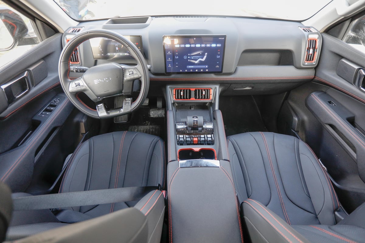 Inside the BYD Shark 6 DMO, a sleek and tech-forward cabin features a 12.8-inch rotating touchscreen and premium leather seats with bold red stitching.